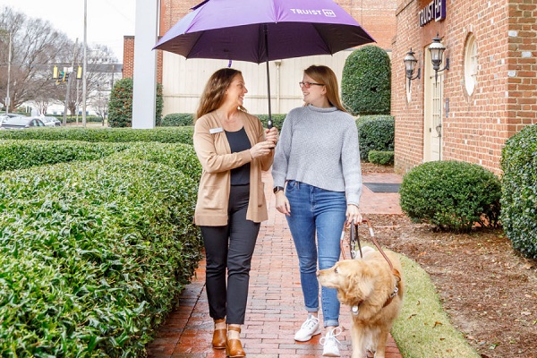 image of two woman under an umbrella with a service dog
