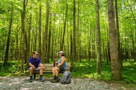 Truist teammate Mark Case sits on a bench surrounded by dense woods, speaking with a fellow female hiker