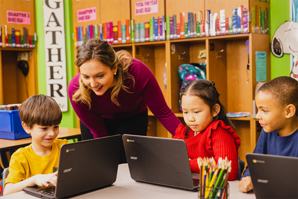 image of teacher working with students on laptops